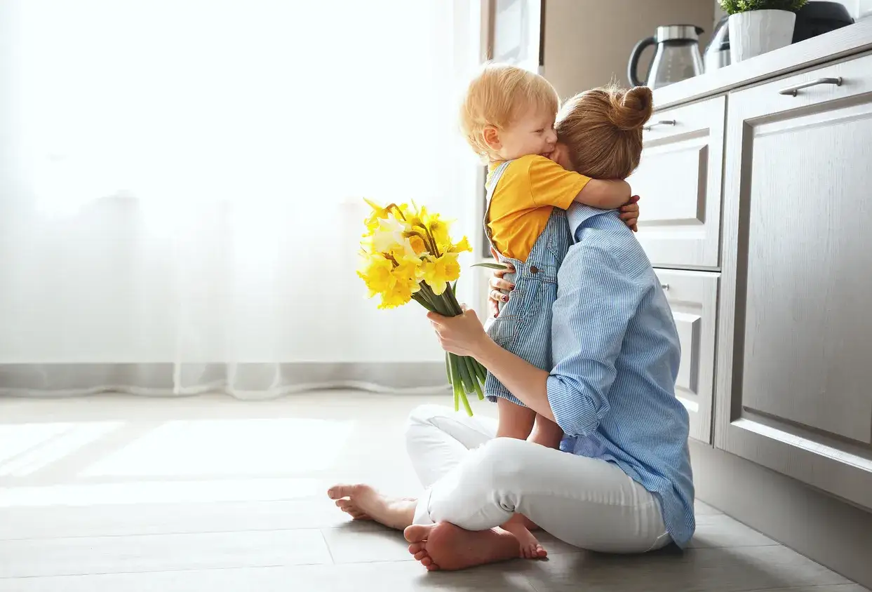Un enfant enlace sa mère, lui offrant un bouquet de jonquilles. Une scène touchante qui illustre l'amour inconditionnel d'une mère.