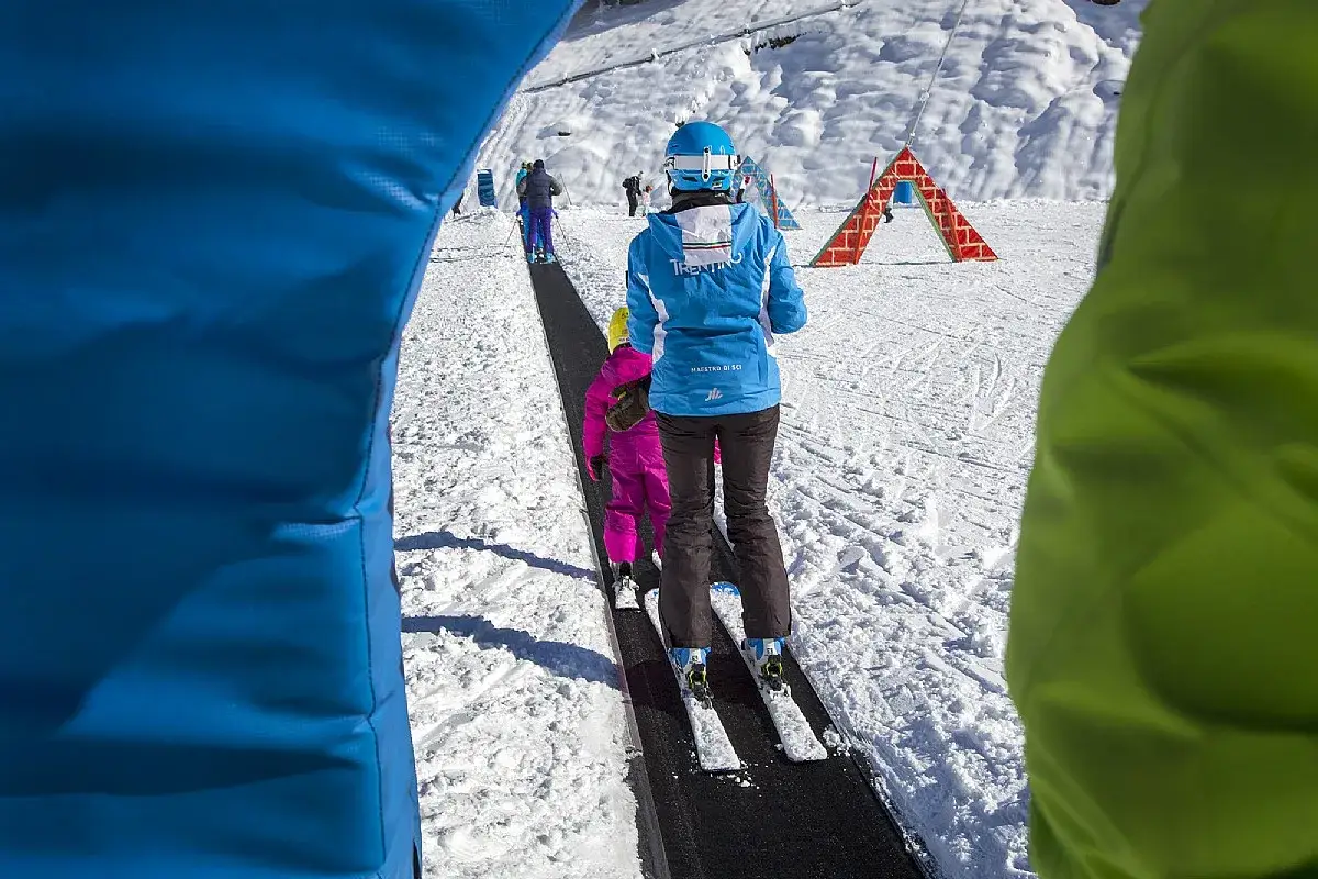 Bambini imparano a sciare su un tapis roulant in montagna, con un maestro di sci che li guida.