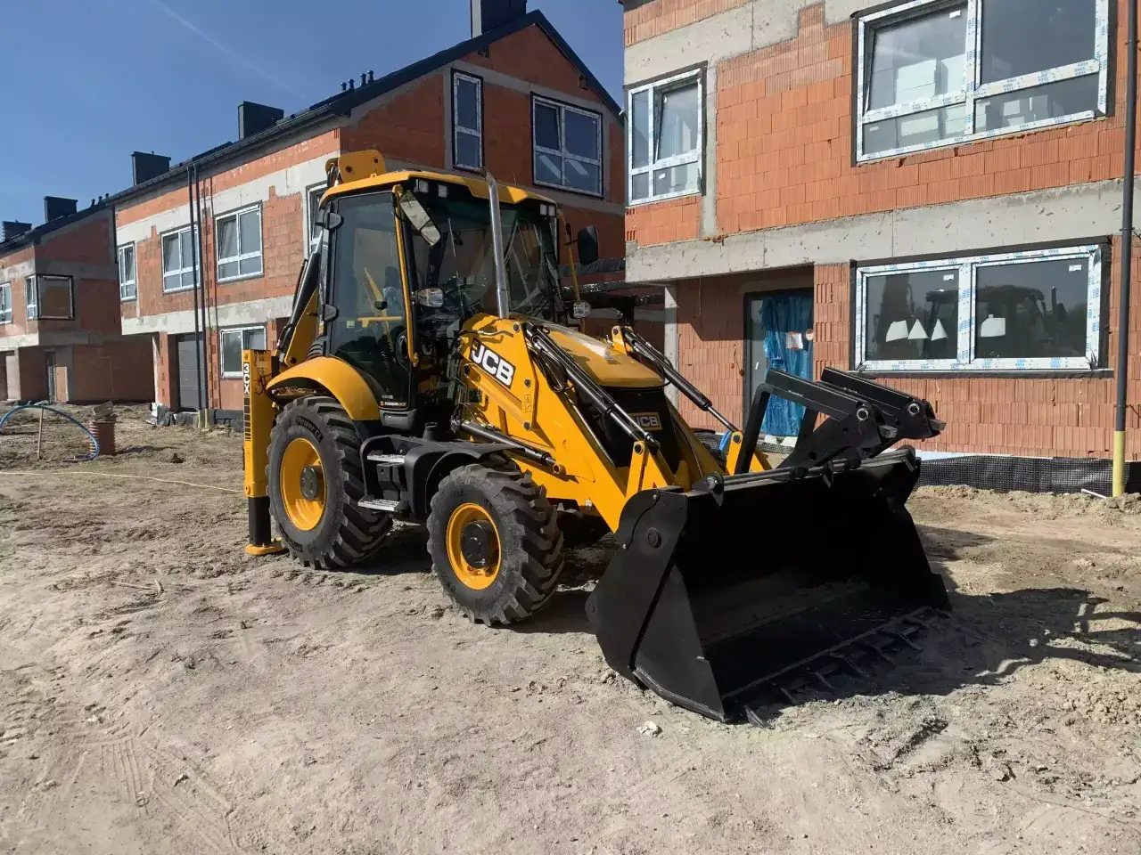 Żółta koparko-ładowarka JCB 3CX na placu budowy, gotowa do pracy. Dane techniczne tej maszyny pozwalają na efektywne prace ziemne.