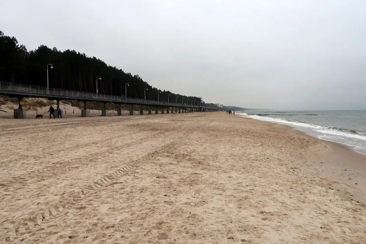 Spacer po plaży w Mielnie poza sezonem. Widać molo, las i morze.