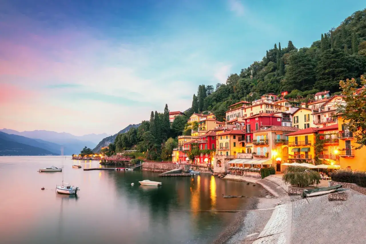 Colorate case aggrappate alla collina sul lago di Garda, con barche che galleggiano sull'acqua calma al tramonto. Un'immagine che cattura le attrazioni del lago di Garda.