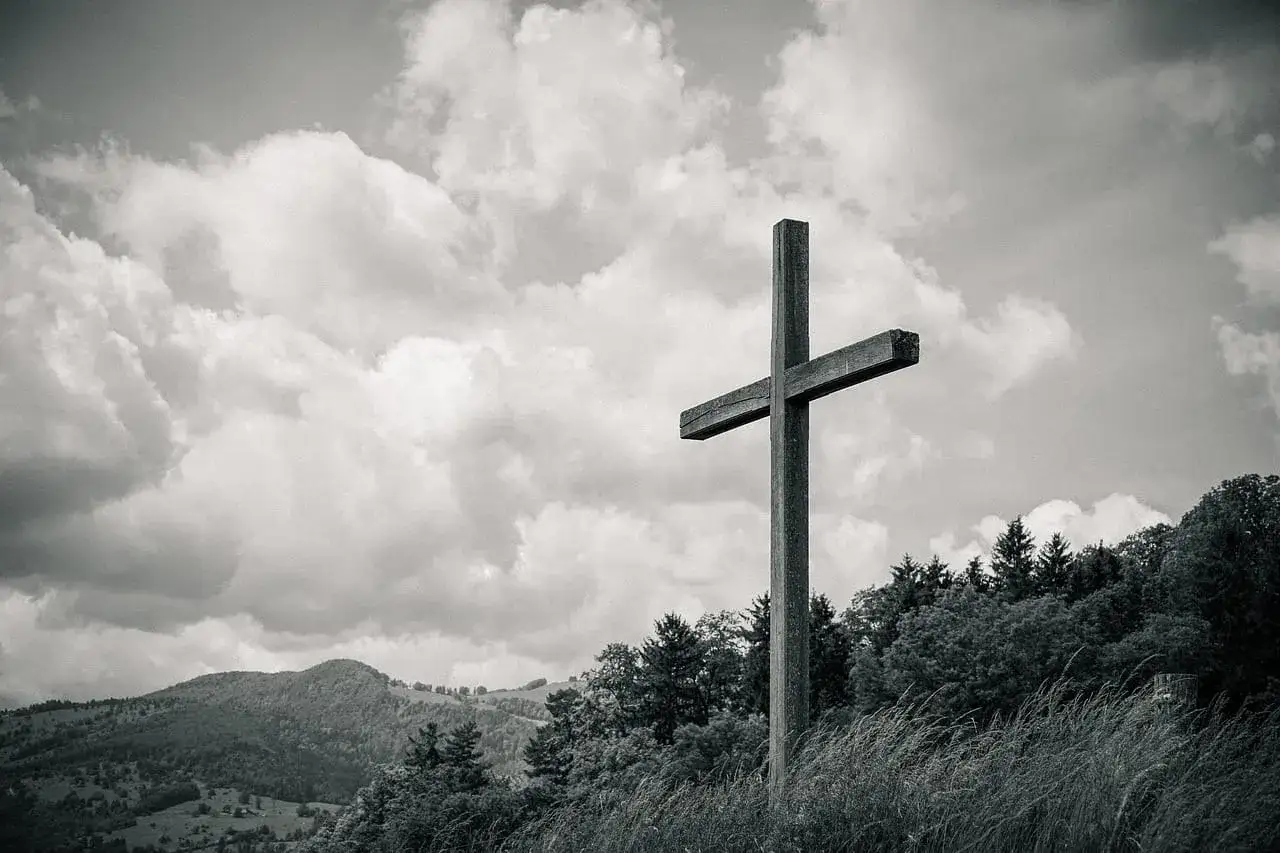 Drewniany krzyż na tle burzowych chmur, wzgórz i lasu. Czasem to właśnie w takich momentach czujemy, że bóg daje znaki.