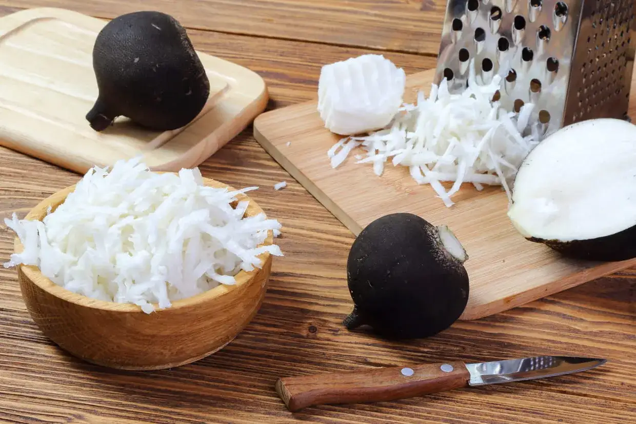 Radis noir r&acirc;p&eacute; pr&ecirc;t pour une recette. Un couteau, une r&acirc;pe et des radis noirs entiers et coup&eacute;s sont dispos&eacute;s sur des planches en bois.
