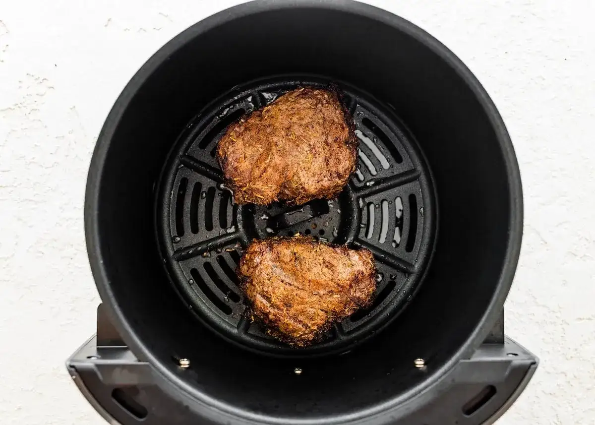 Deux morceaux de filet mignon assaisonnés cuisent dans un panier d'air fryer.
