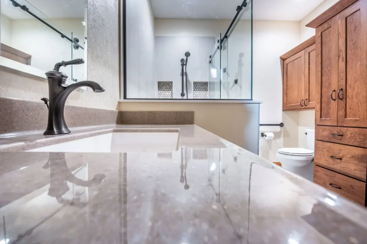 Bagno moderno con lavabo in quarzo lucido, doccia a vista e mobili in legno. Il **pavimento facile da pulire** completa l'ambiente.