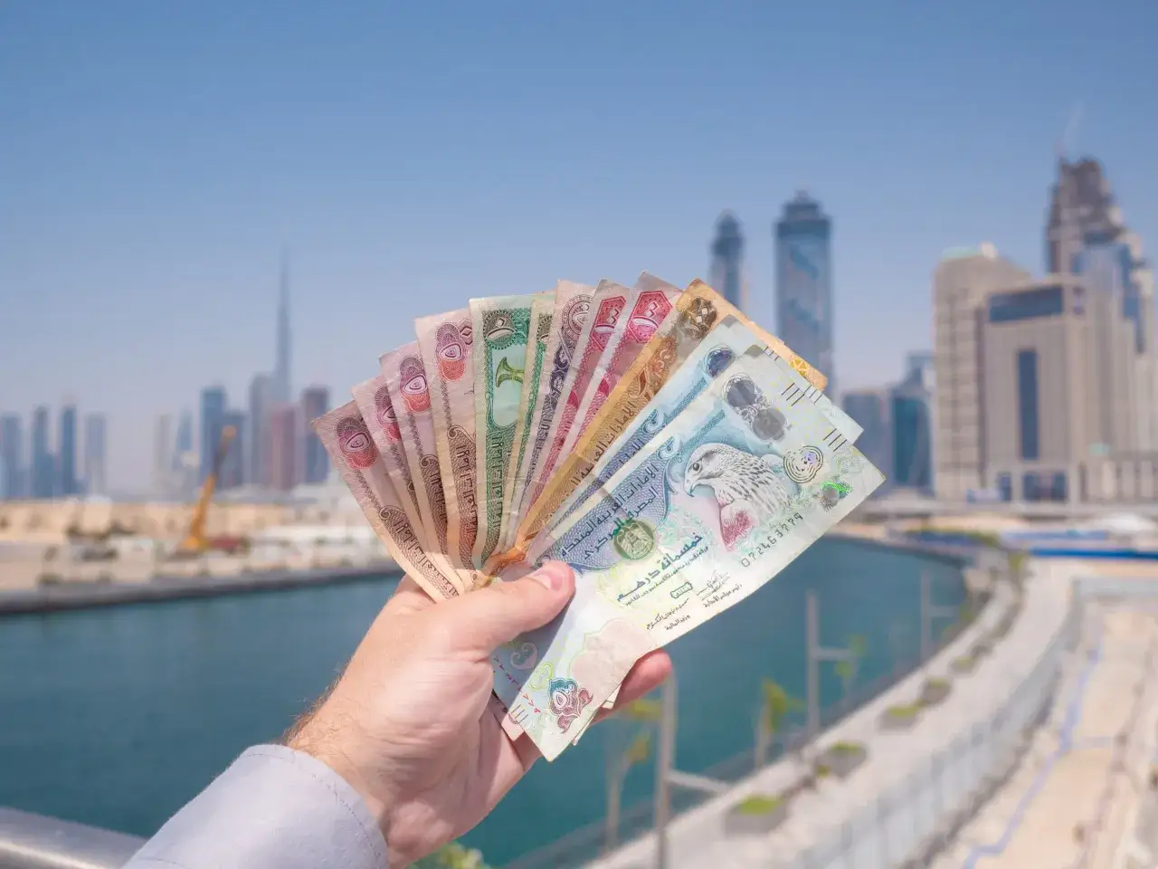 Dłoń trzyma wachlarz banknotów. To dirham Zjednoczonych Emiratów Arabskich, czyli jaka waluta jest w Dubaju.