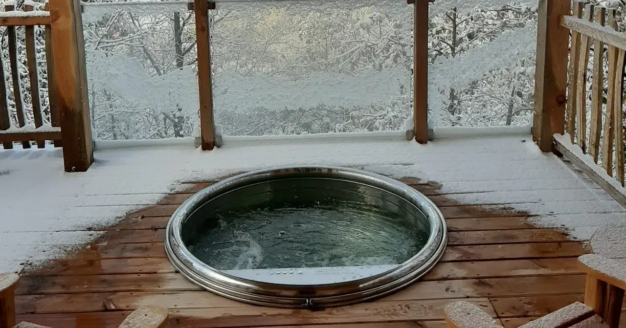 Jacuzzi fumant sur une terrasse enneig&eacute;e, un lieu insolite dans le Jura, offrant un contraste saisissant entre le froid ext&eacute;rieur et la chaleur de l'eau.
