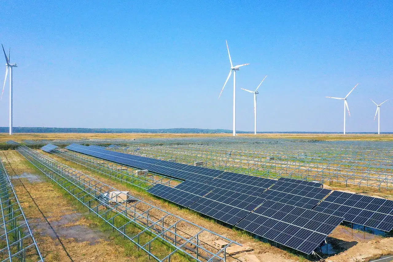 Rozległe **elektrownie słoneczne w Polsce** z rzędami paneli i wiatrakami na horyzoncie, symbolizujące zieloną energię.
