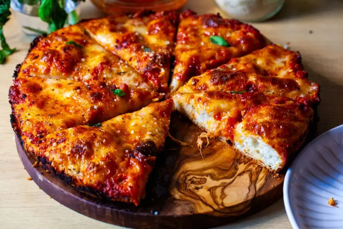 Pyszna pizza z patelni, pokrojona na kawałki, z ciągnącym się serem i aromatycznym sosem pomidorowym.