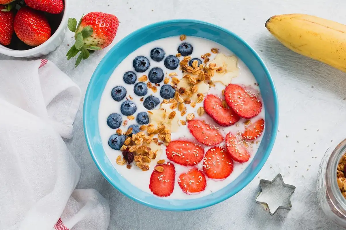 Ciotola azzurra con yogurt, mirtilli, fragole, banana e granola. Una colazione sana per bambini, piena di energia e gusto.