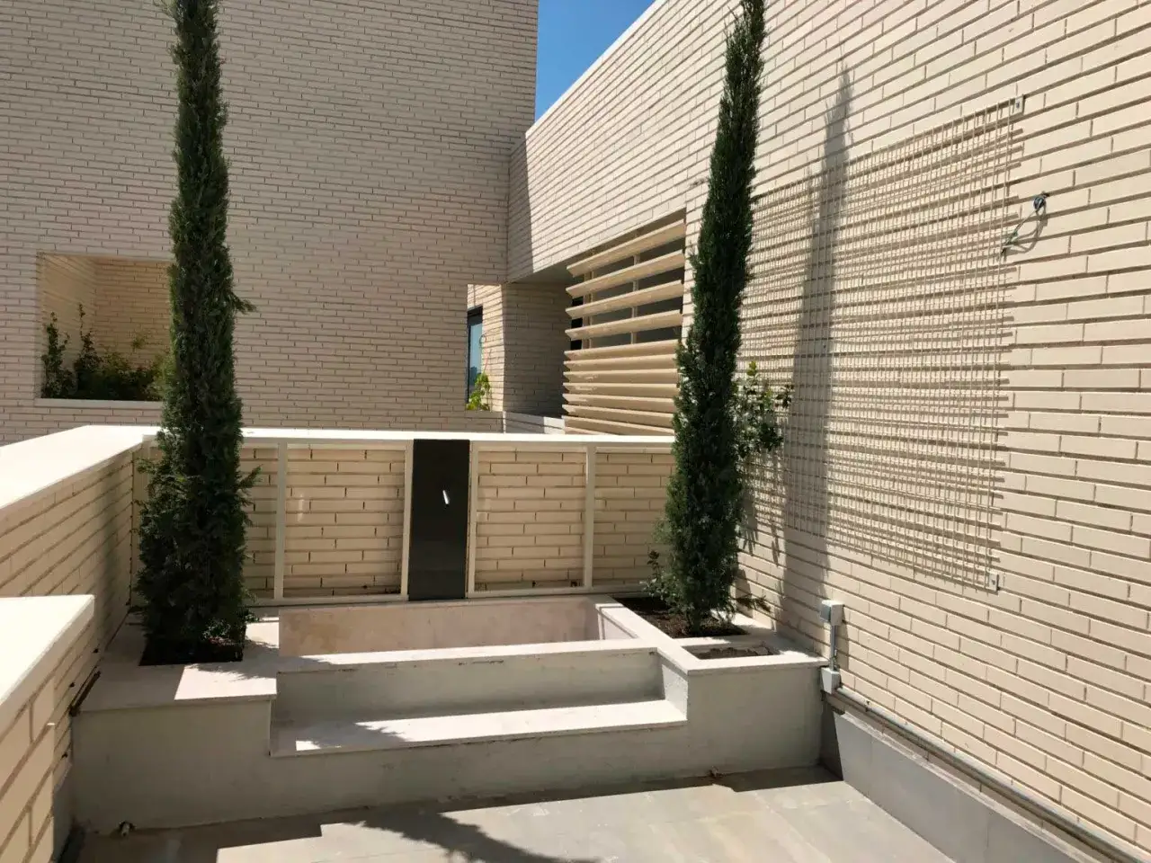 Terraza moderna con cipreses y un retranqueo de fachada que crea un espacio &iacute;ntimo.