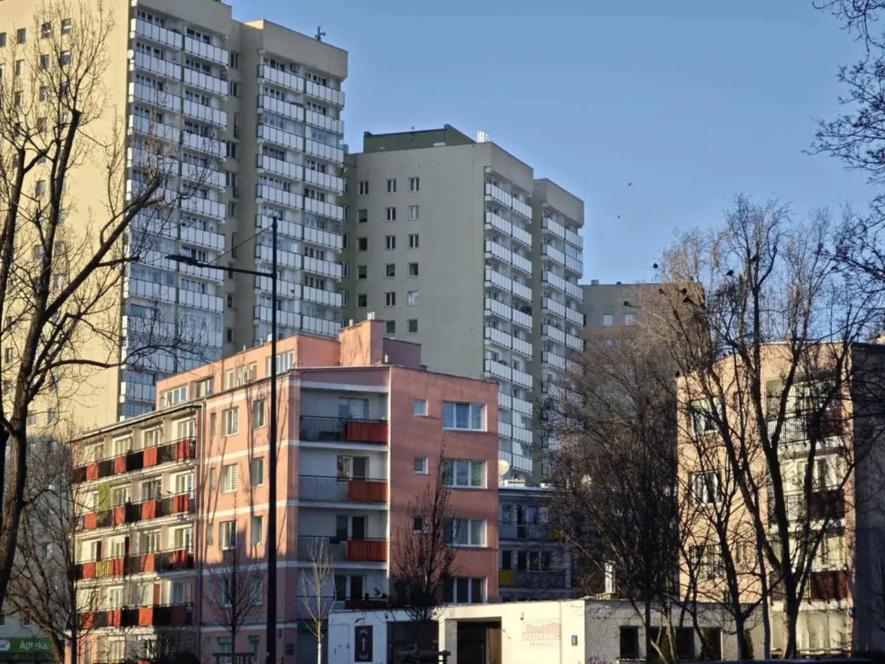 Bloki mieszkalne w słońcu. W tle wysokie budynki, z przodu niższy, różowy. To widok, który przypomina o tym, co to jest czynsz administracyjny.