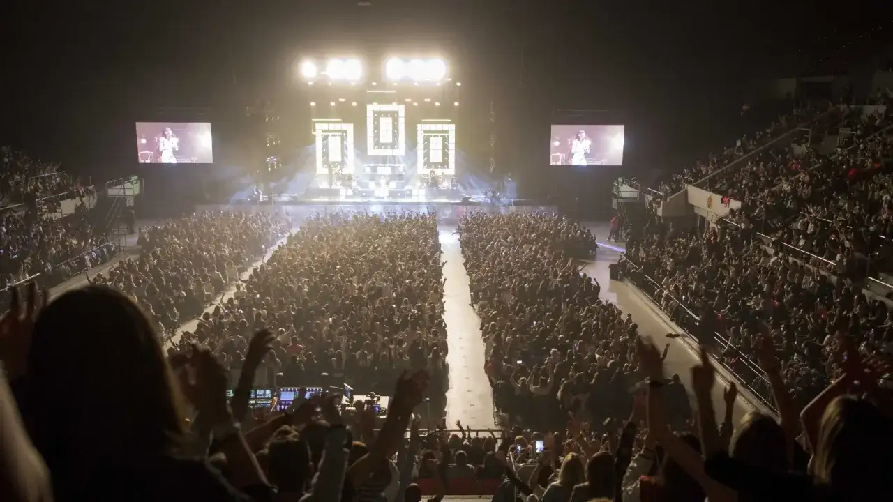 Multitud en concierto de Aitana en Zaragoza, con pantallas gigantes mostrando a la artista y luces brillantes.