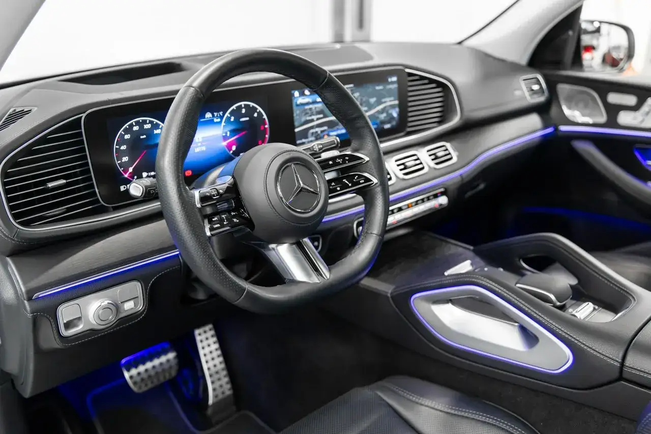 Wnętrze luksusowego **Mercedes GLE 450** z podświetleniem ambientowym. Widoczna kierownica, cyfrowe zegary i konsola środkowa.