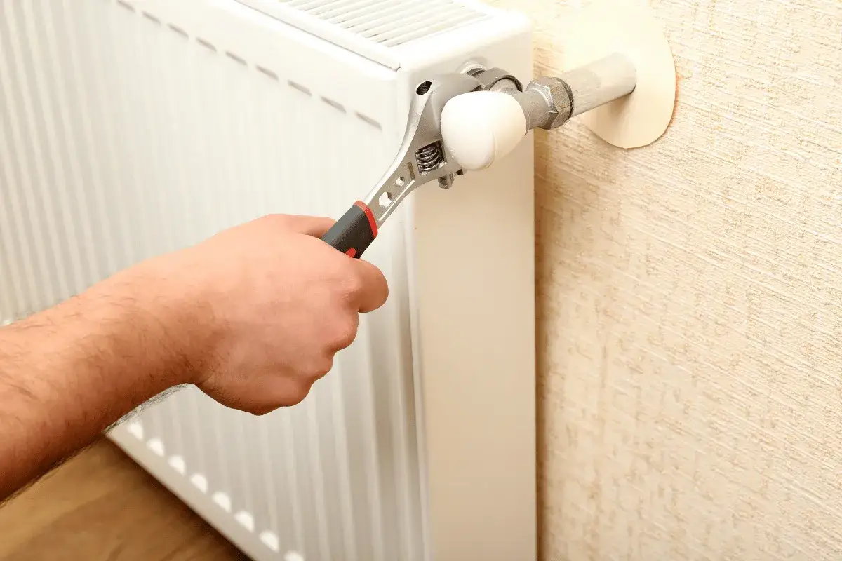 Mano con chiave inglese che regola la valvola di un termosifone bianco. L'aria nei termosifoni &egrave; un problema comune.