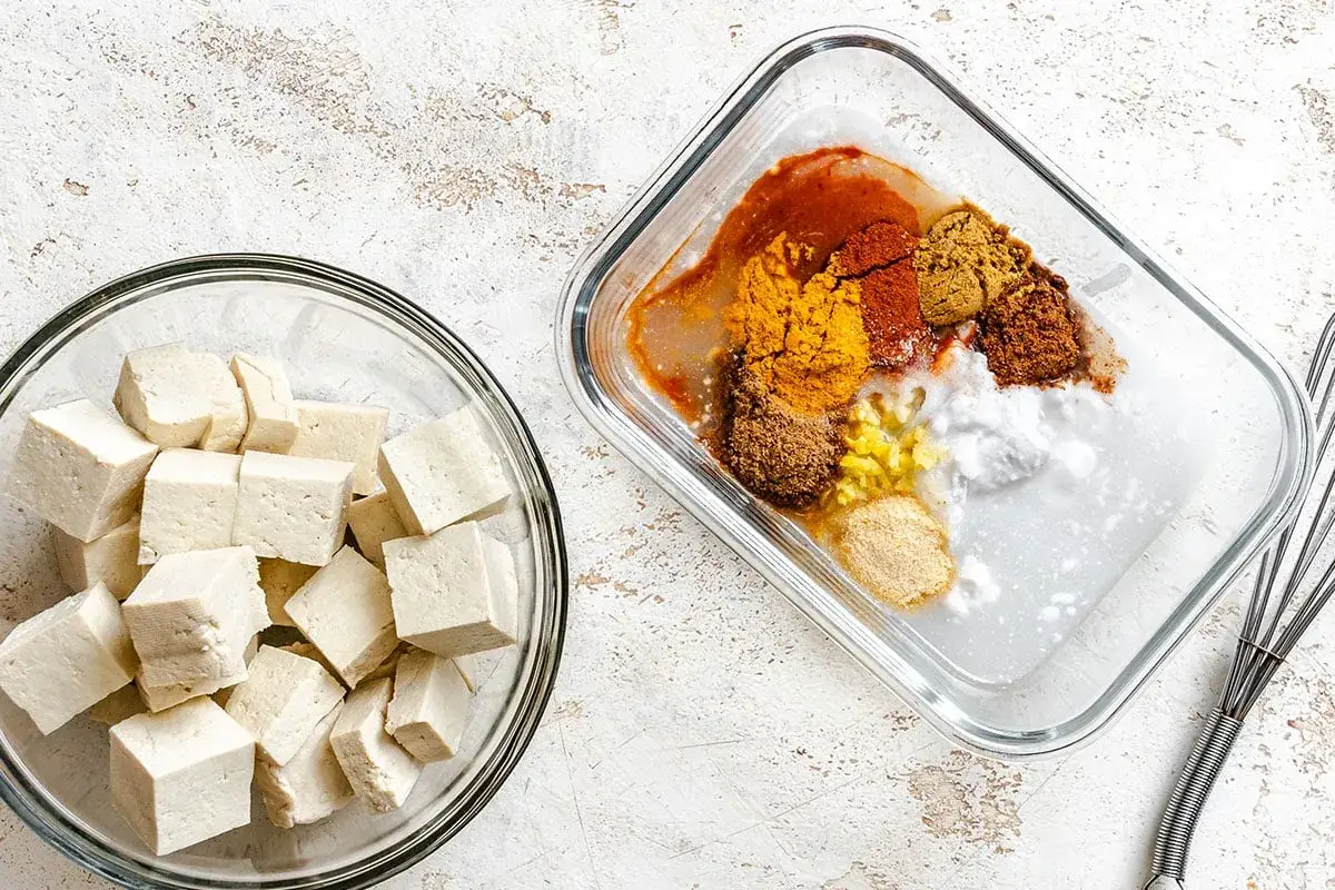 Würfel von Tofu in einer Schüssel, daneben eine Marinade mit Gewürzen wie Kurkuma und Paprika, bereit zum Tofu marinieren.