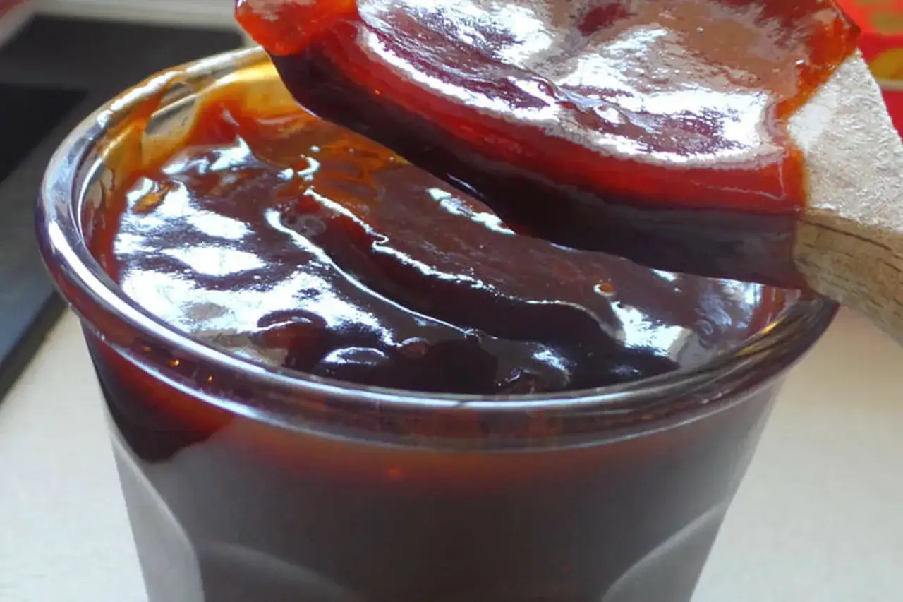 Une cuillère en bois prélève une sauce barbecue épaisse et brillante d'un pot en verre. Parfait pour votre prochaine recette de sauce barbecue.