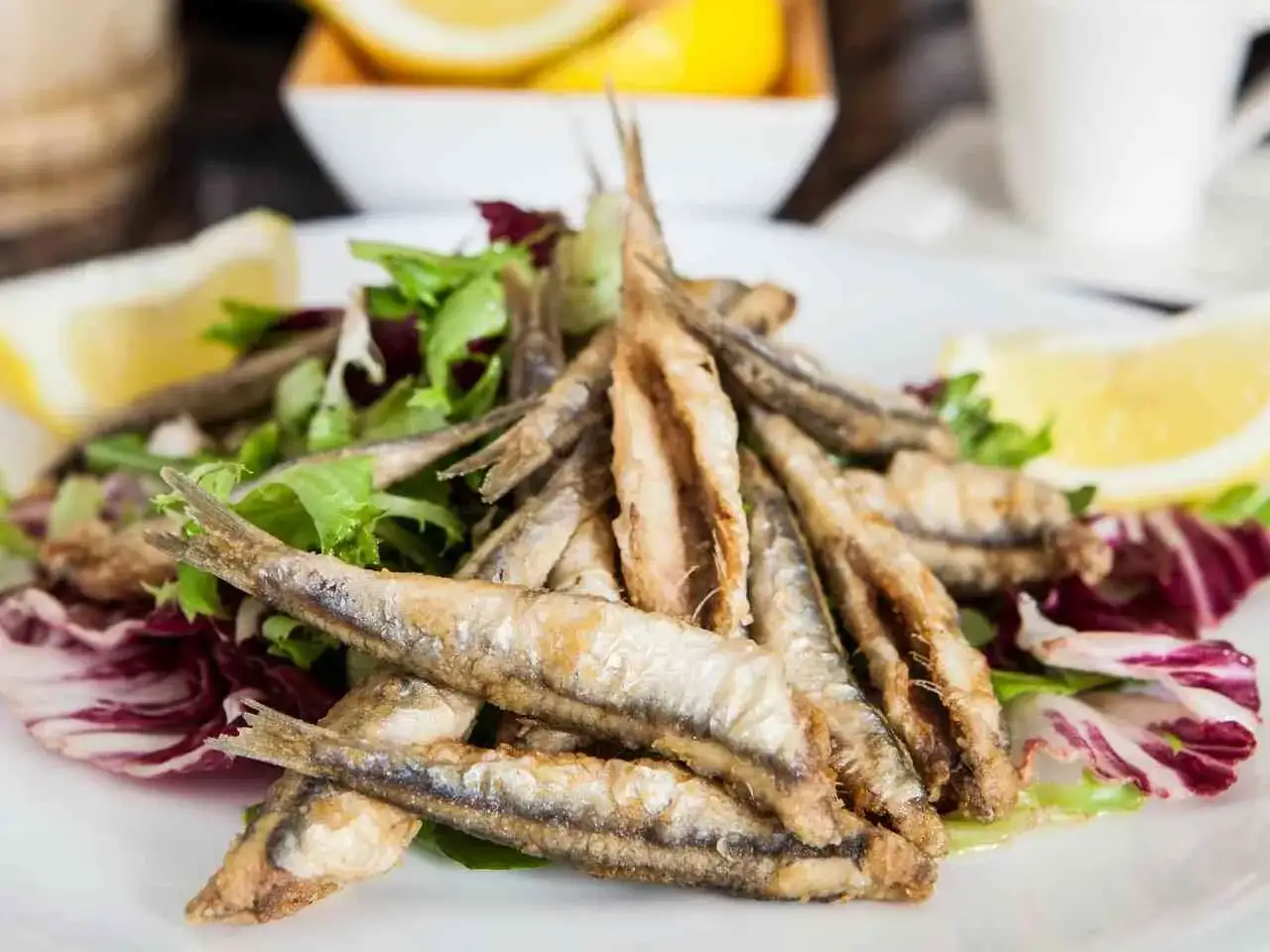 Mont&oacute;n de boquerones fritos crujientes sobre una cama de lechugas variadas y radicchio, acompa&ntilde;ados de gajos de lim&oacute;n.