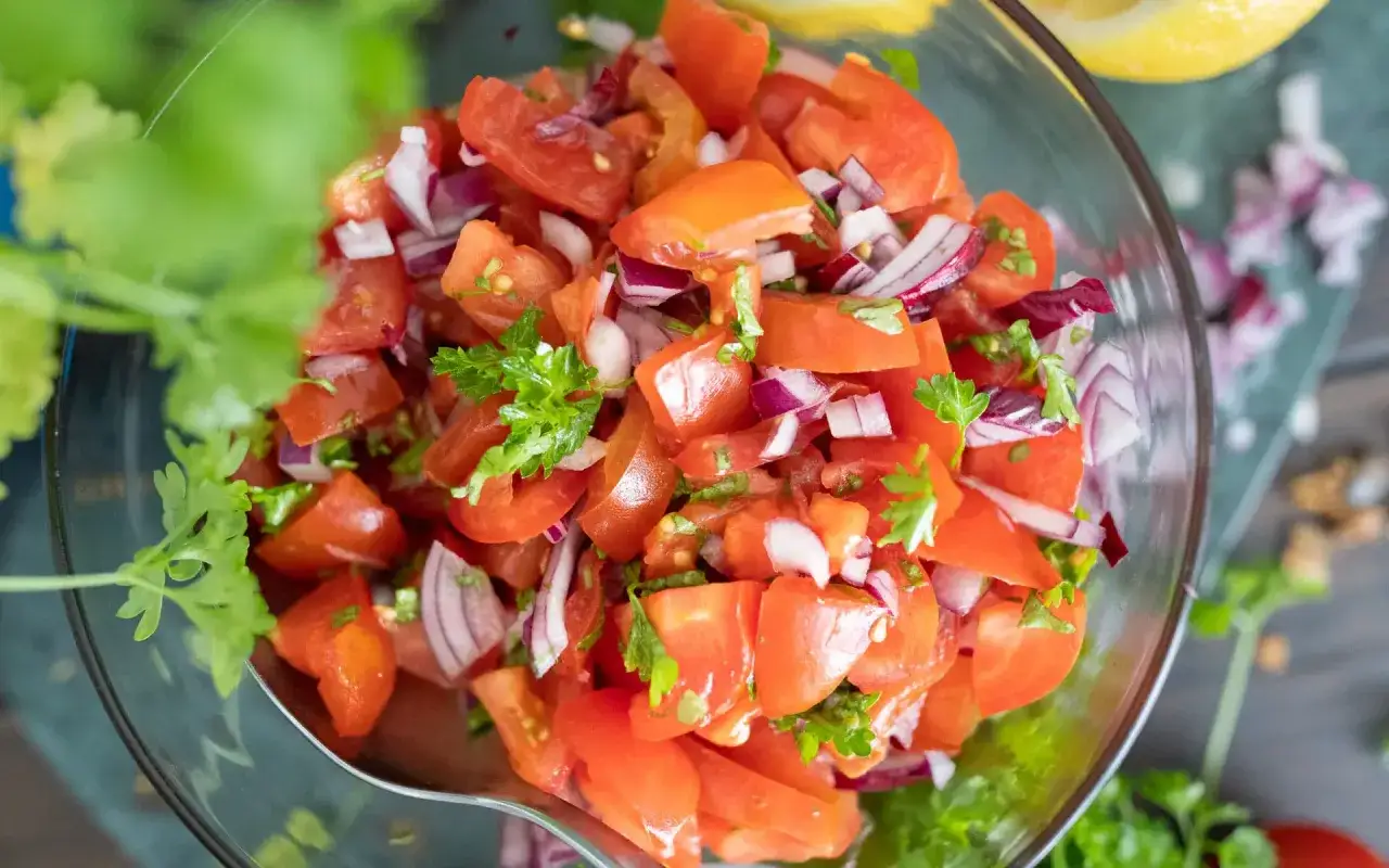 Frischer tomatensalat mit zwiebeln und Petersilie in einer Glassch&uuml;ssel, garniert mit Koriander.