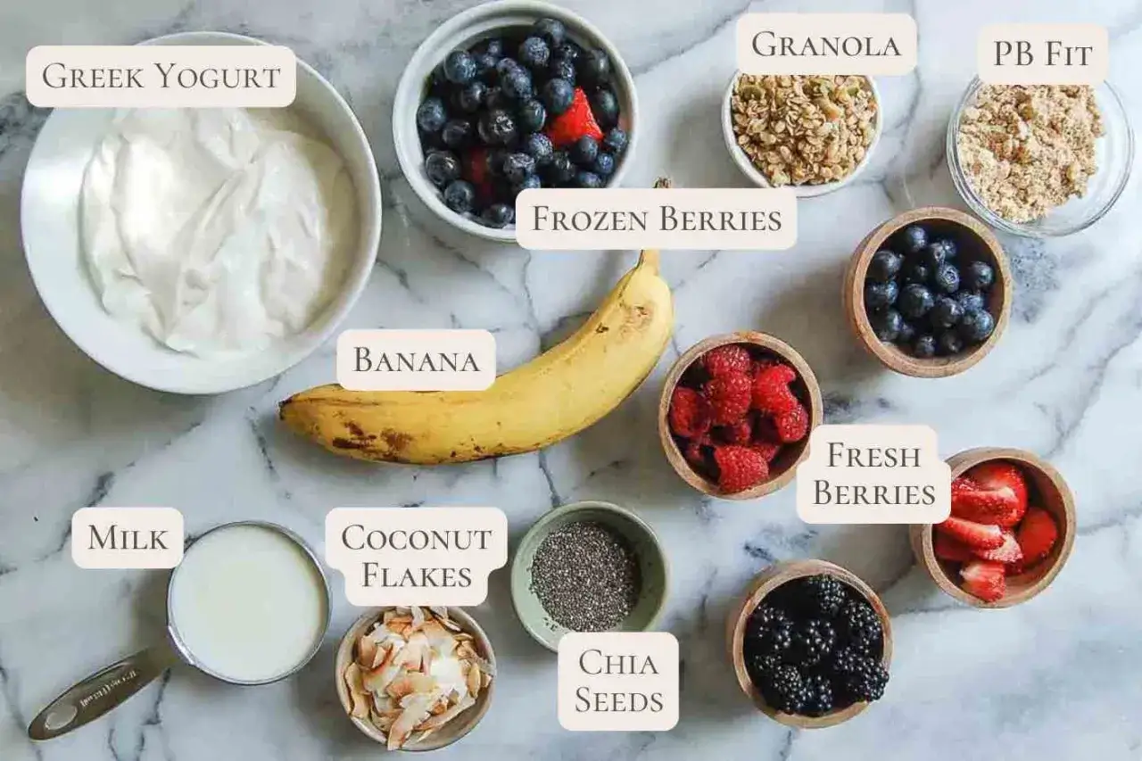 Ingredienser för ett gott smoothie recept: grekisk yoghurt, banan, frysta bär, mjölk, kokosflingor, chiafrön, färska bär, granola och PB Fit.