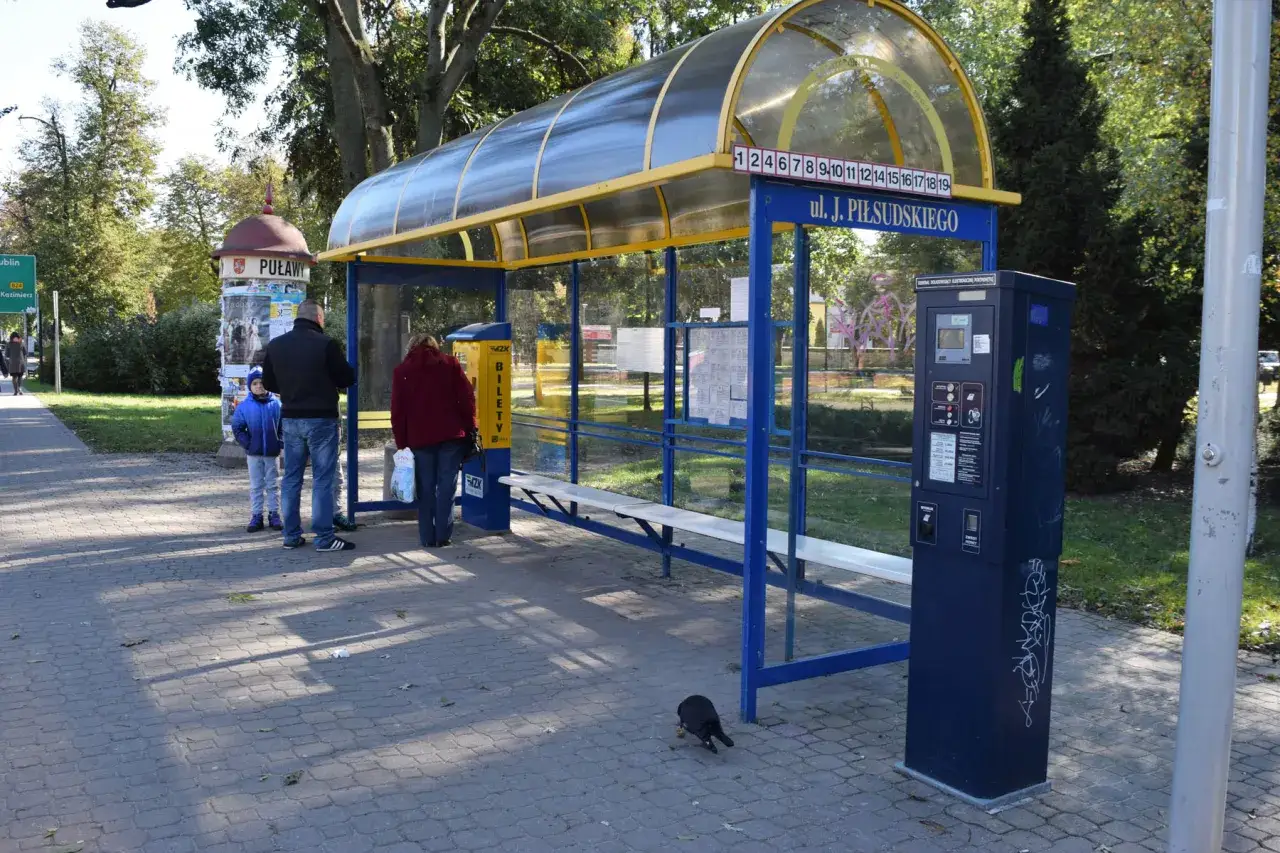 Przystanek autobusowy z rozkładem jazdy autobusu 102. Ludzie czekają na ul. Piłsudskiego.