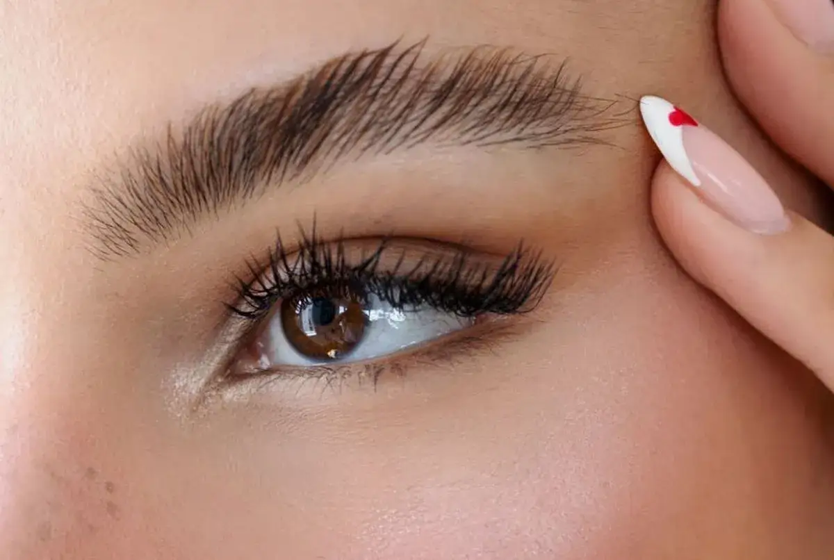 Un &oelig;il marron aux cils longs et fournis, sublim&eacute; par un maquillage discret. Un ongle manucur&eacute; avec un c&oelig;ur rouge attire le regard.