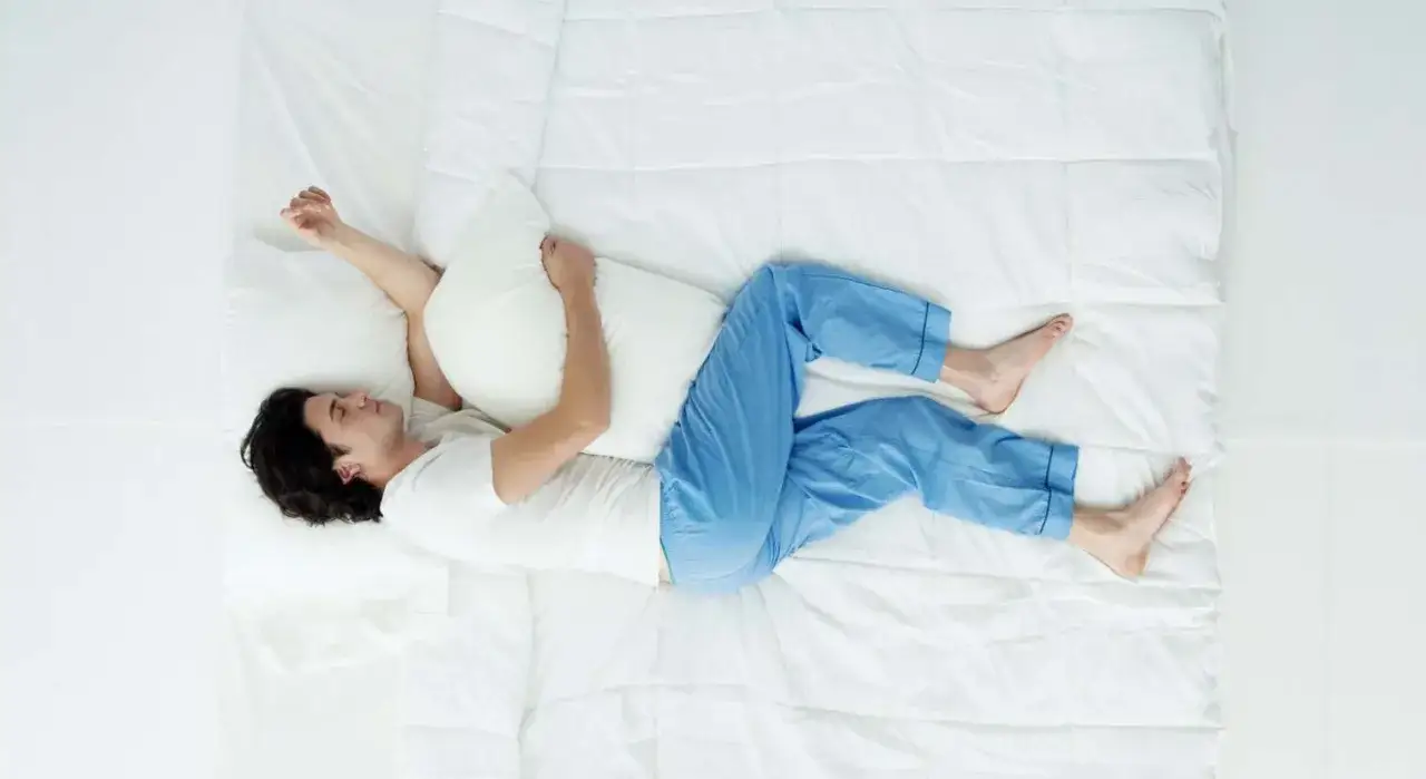 Hombre durmiendo de lado con almohada entre las piernas, demostrando como dormir de lado correctamente para un descanso óptimo.