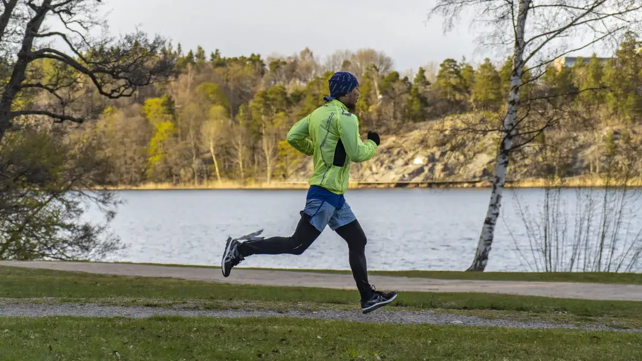 Man i ljusgrön jacka springer längs en sjö, en perfekt dag att springa en mil om dagen i svensk natur.