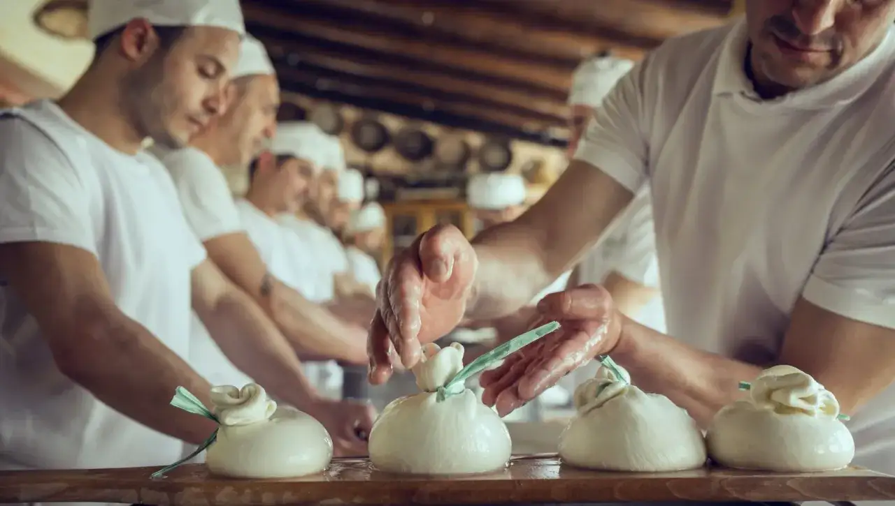 Artigiani creano burrata, scoprendo l'origine di questo formaggio fresco. Mani esperte modellano la pasta filata, legandola con fili verdi.