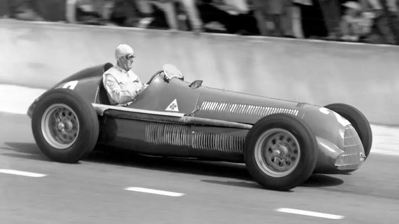 Kierowca w kasku i goglach ściga się w historycznym bolidzie Alfa Romeo F1.