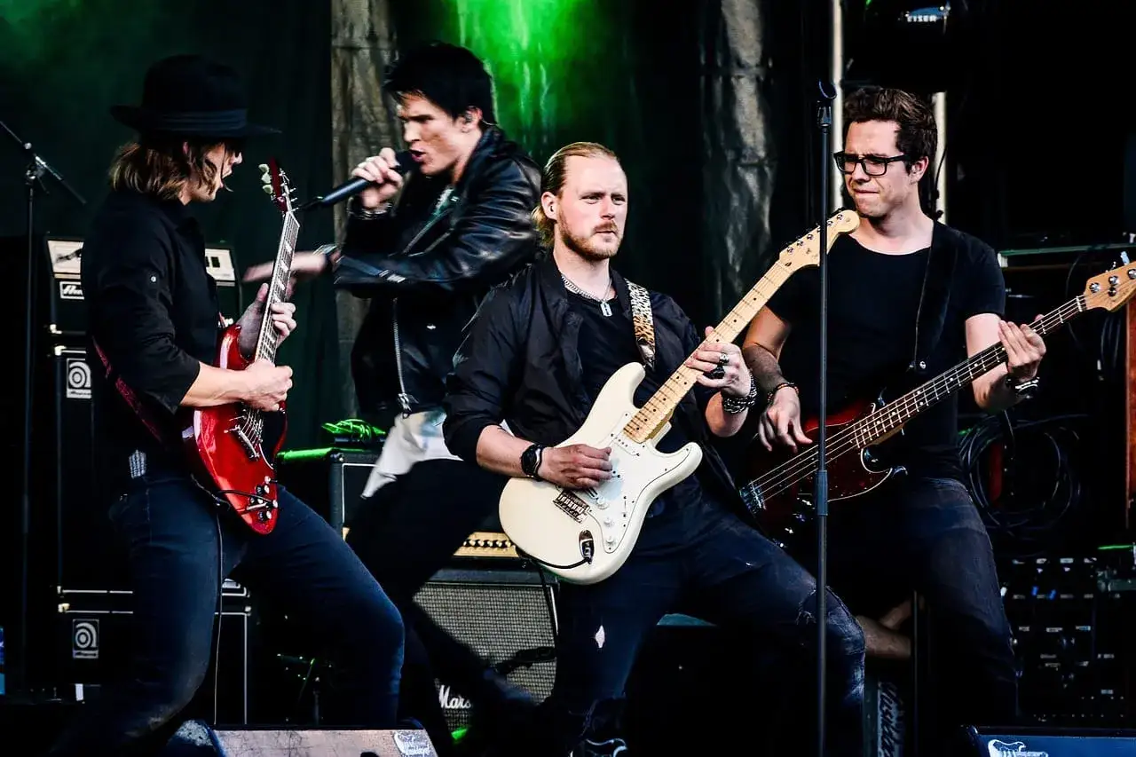 Zespół gra na scenie, gitarzyści i basista tworzą muzykę do najpopularniejszych piosenek.