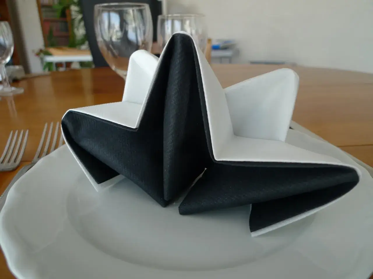 Pliage serviette accord&eacute;on 2 couleurs, noir et blanc, formant une &eacute;toile sur une assiette blanche.
