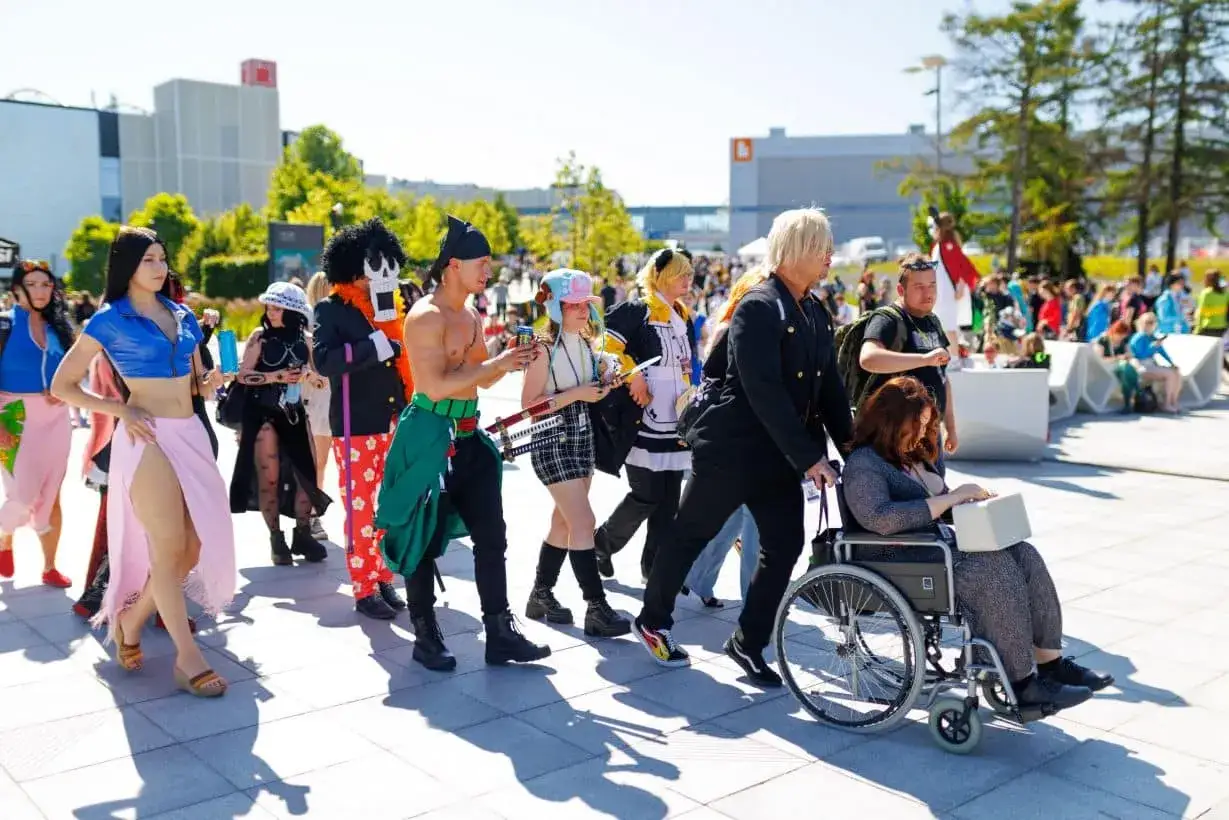 Grupa cosplayerów, w tym postacie z anime, idzie ulicą. Wśród nich widać osoby z pyrkon tokeny.