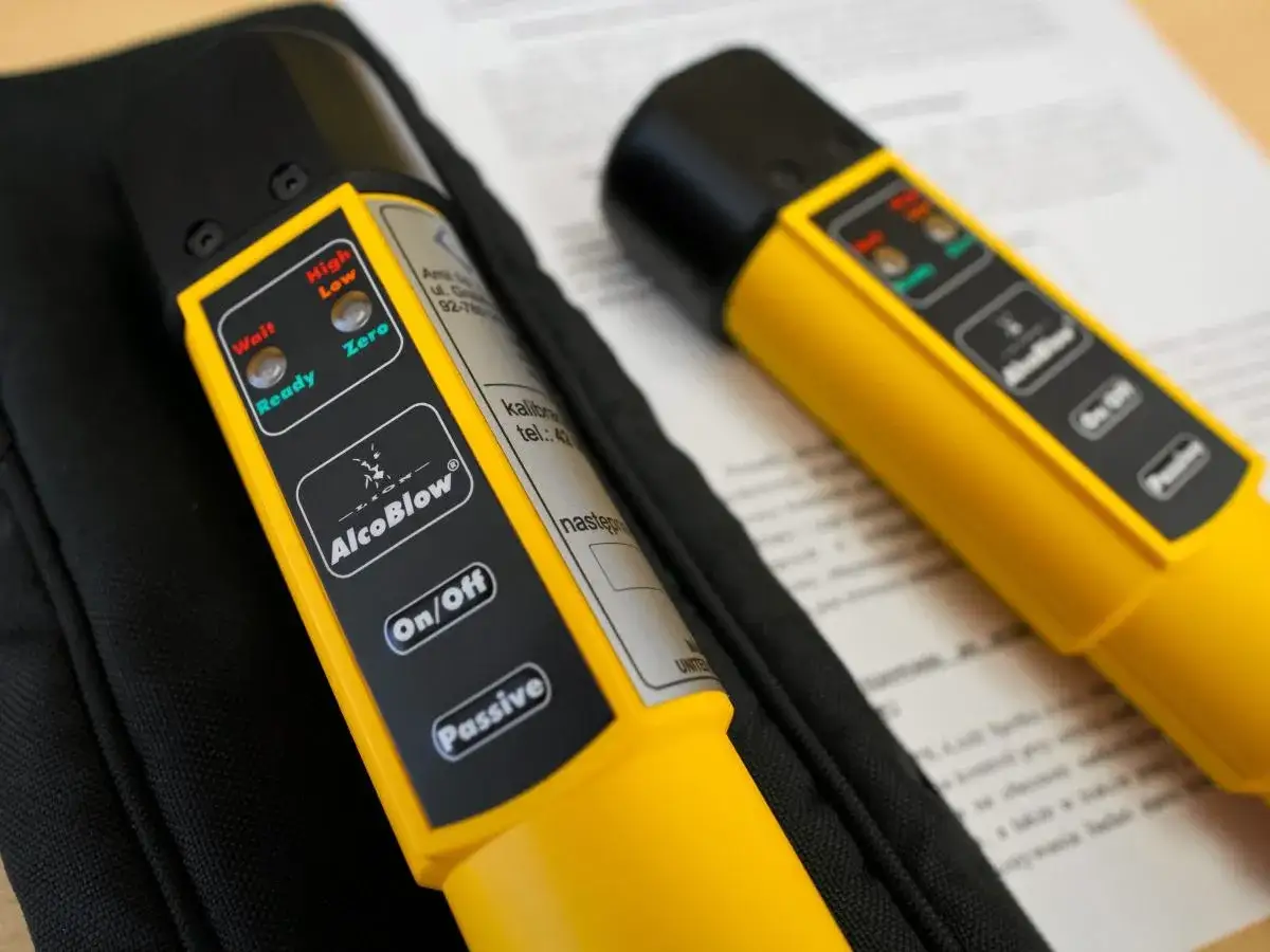 Dwa alkomaty AlcoBlow leżą na dokumentach. Jeden pokazuje