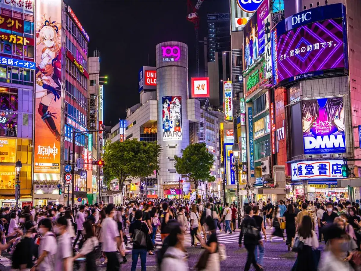 Tłum ludzi na ruchliwym skrzyżowaniu w Tokio, otoczony neonowymi reklamami. Obraz sugeruje, ile ludzi mieszka w Tokio, pokazując jego tętniące życiem centrum.