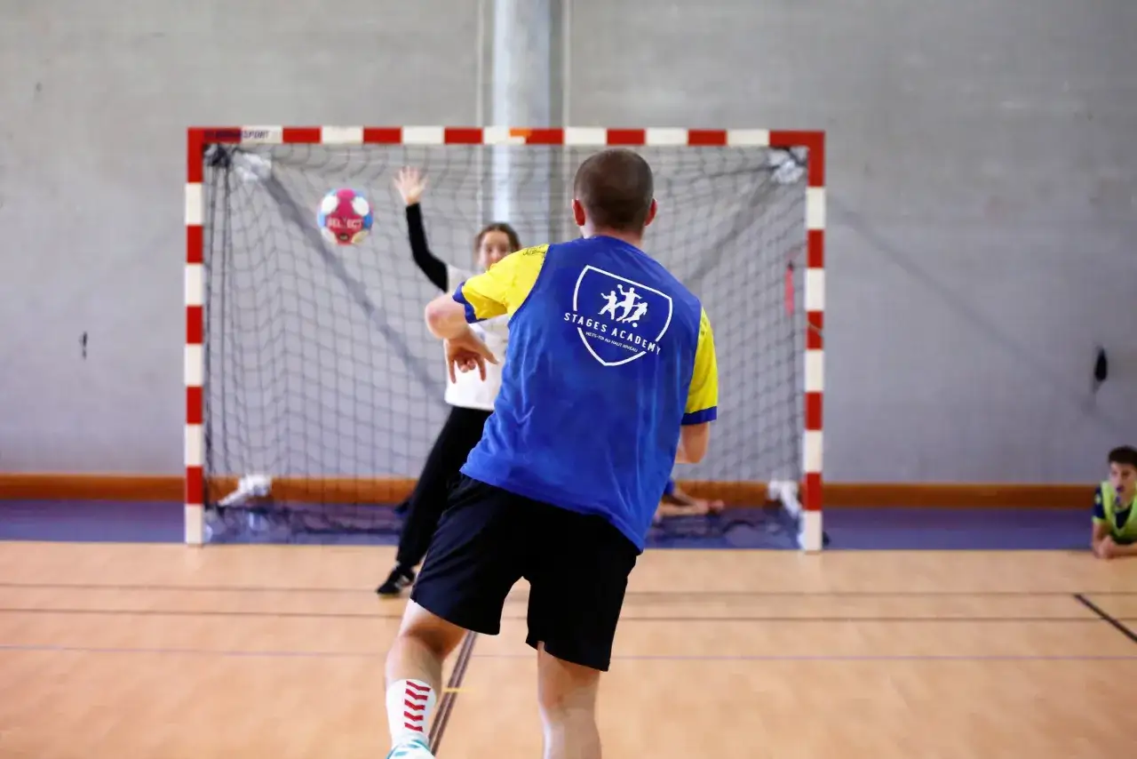 Des jeunes s'entraînent au handball pendant les vacances scolaires Haute Garonne. Un joueur lance le ballon vers le but.
