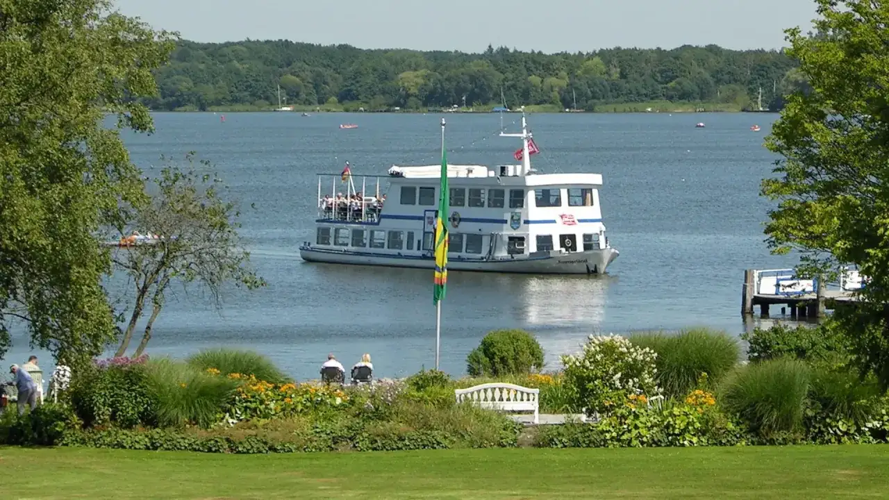 Ein Ausflugsschiff fährt auf dem Zwischenahner Meer, umgeben von grünen Ufern und blühenden Blumen.