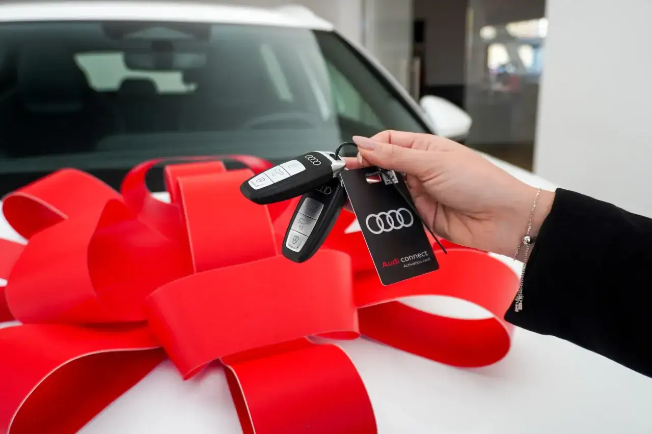 Radość z odbioru nowego Audi! Kluczyki do samochodu i karta Audi connect na tle czerwonej kokardy. To prawdziwa ulga na samochód!