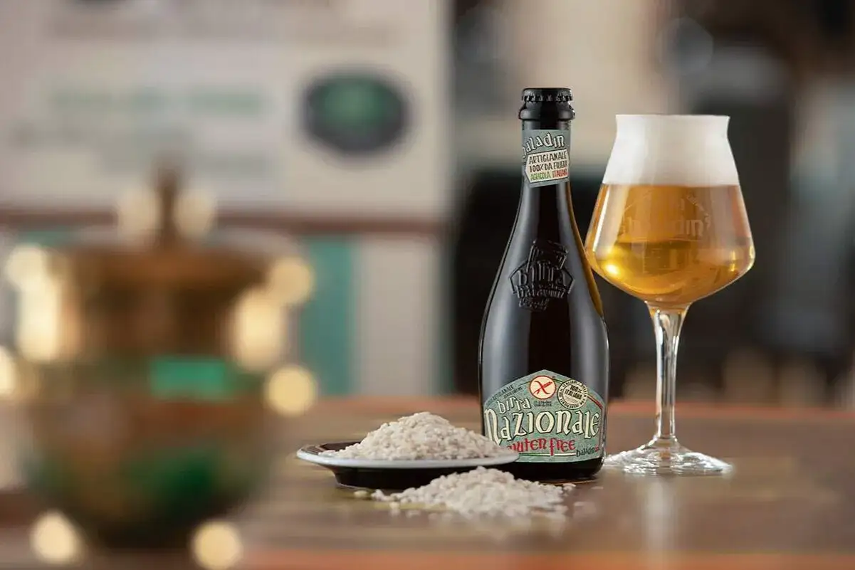Birra Nazionale, una birra artigianale senza glutine, perfetta per celiaci. Accanto, un bicchiere colmo e chicchi di riso.