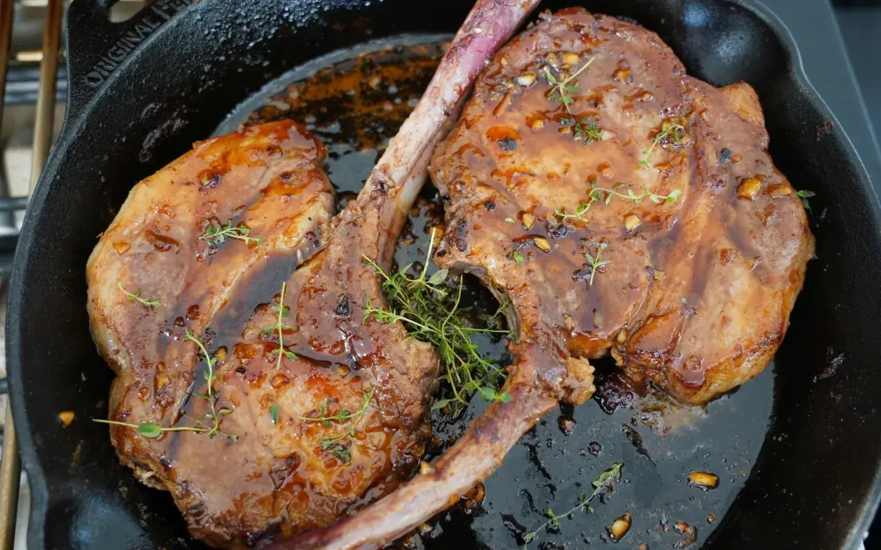 Zwei saftige Koteletts mit Knochen in einer Gusseisenpfanne, glasiert und mit Thymian garniert. Ein köstliches Kotelett Rezept!