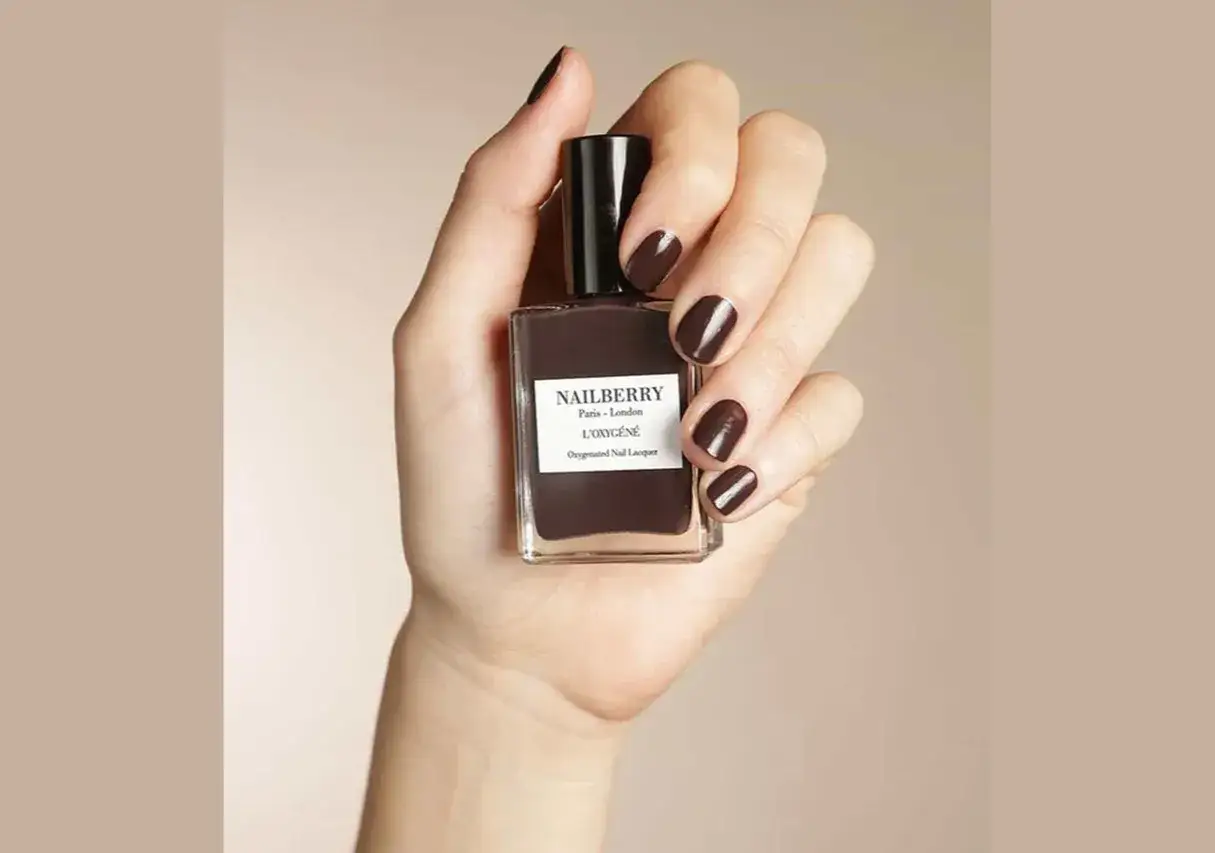 En hand h&aring;ller en flaska m&ouml;rkt, chokladbrunt Nailberry nagellack. Naglarna &auml;r m&aring;lade i samma djupa f&auml;rg.