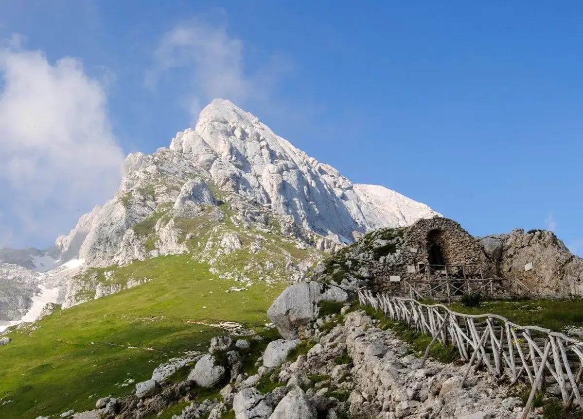 Sentiero di trekking sul Gran Sasso, con un rifugio in pietra e un cielo azzurro.