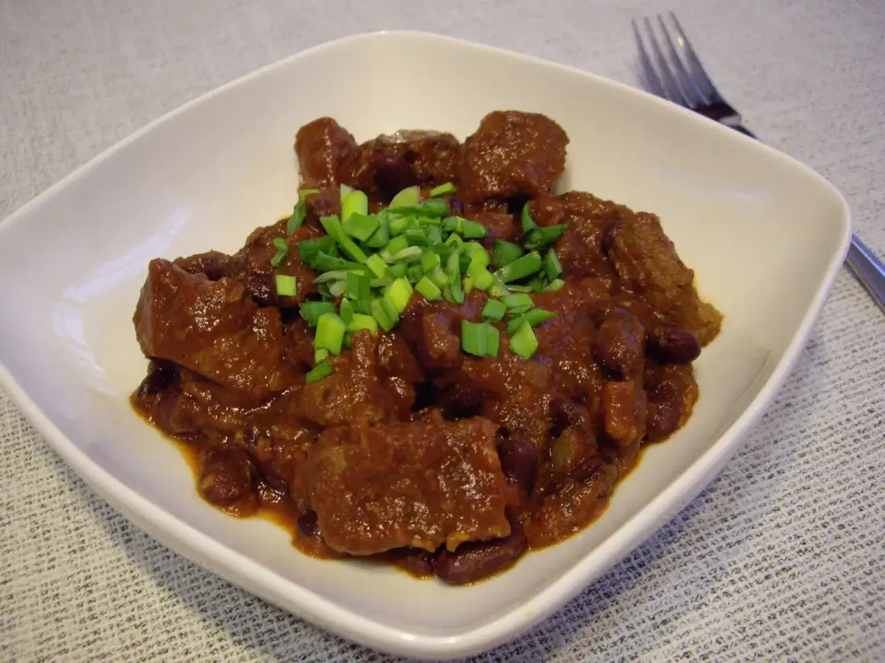 Gęste, aromatyczne chili con carne z kawałkami mięsa i fasolą, posypane szczypiorkiem. Idealne na rozgrzewający posiłek.