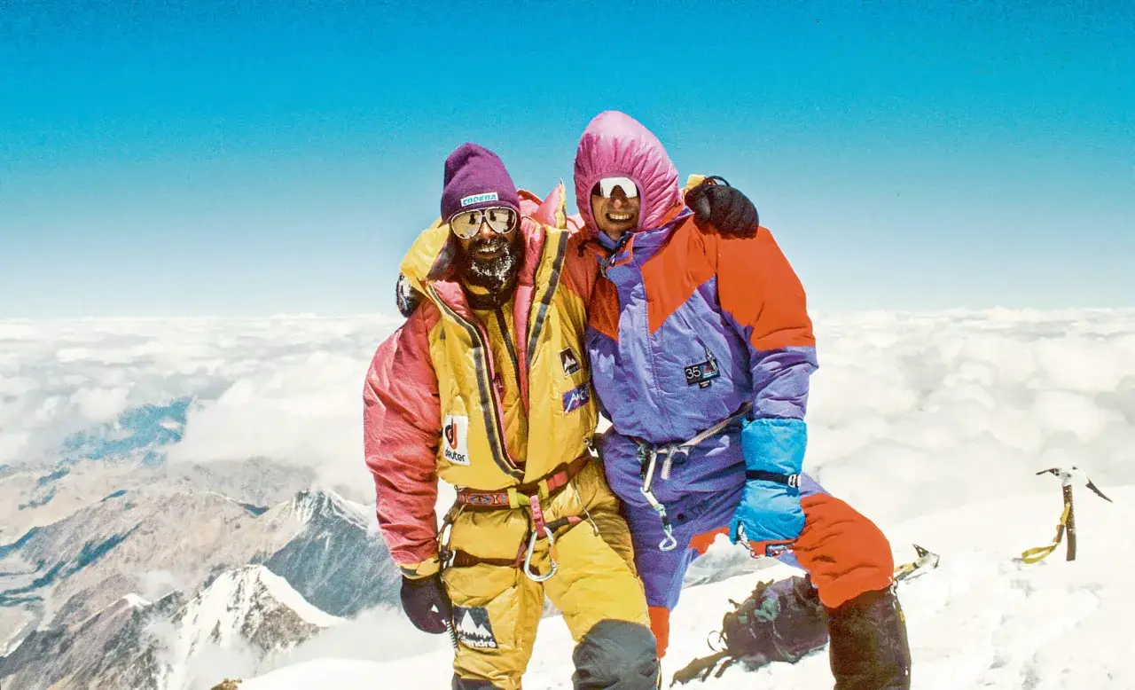 Kami Rita und sein Bergsteigerkollege auf dem Gipfel, umgeben von Wolken und eisigen Gipfeln.
