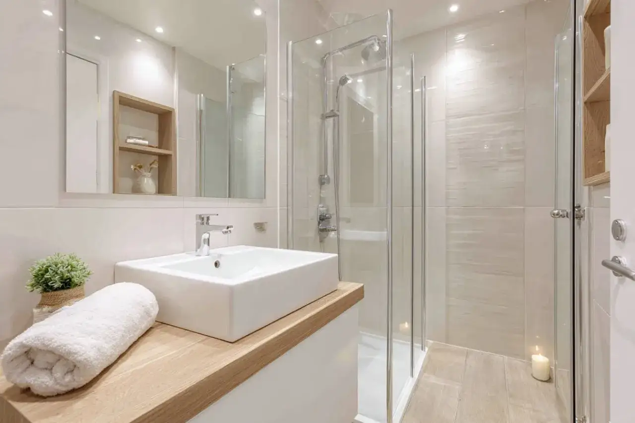 Salle de bain aménagée avec une douche moderne, un lavabo épuré et des touches de bois. Une serviette blanche et une plante apportent de la douceur.