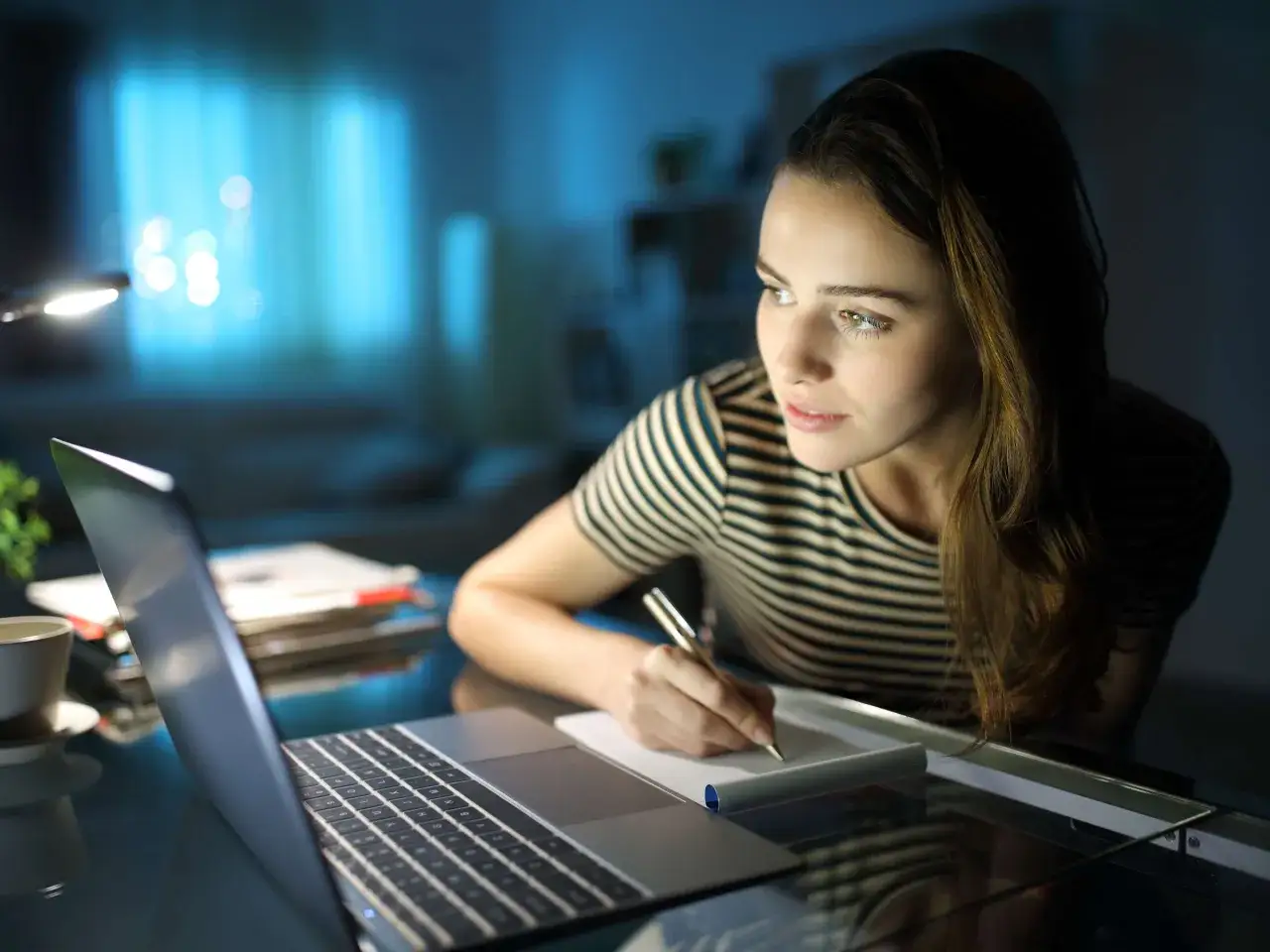 Junge Frau lernt abends am Laptop f&uuml;r ihr Fachabitur im Fernstudium. Sie schreibt Notizen in ein Heft.