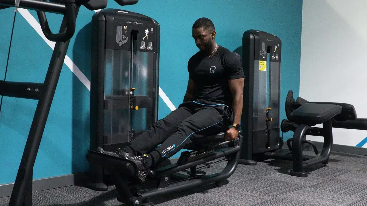 Hombre entrenando gemelos sentado en máquina de gimnasio.