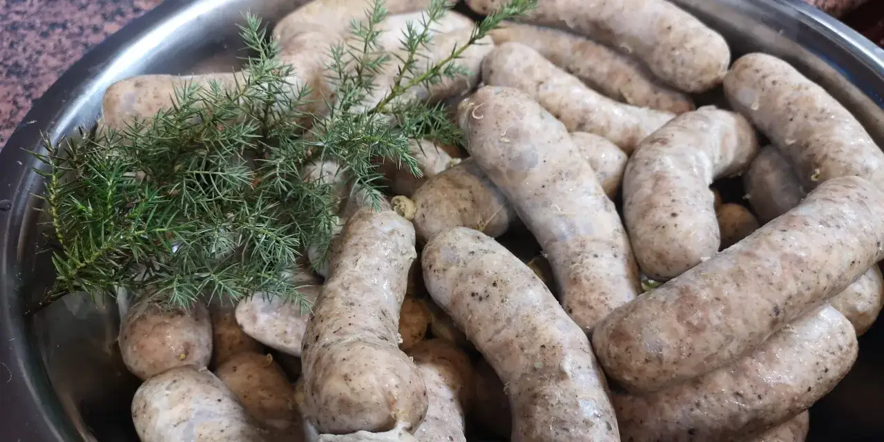Biała kiełbasa w metalowej misce, ozdobiona gałązką jałowca. Idealna na świąteczny stół, zgodnie z tradycyjnym przepisem na białą kiełbasę.