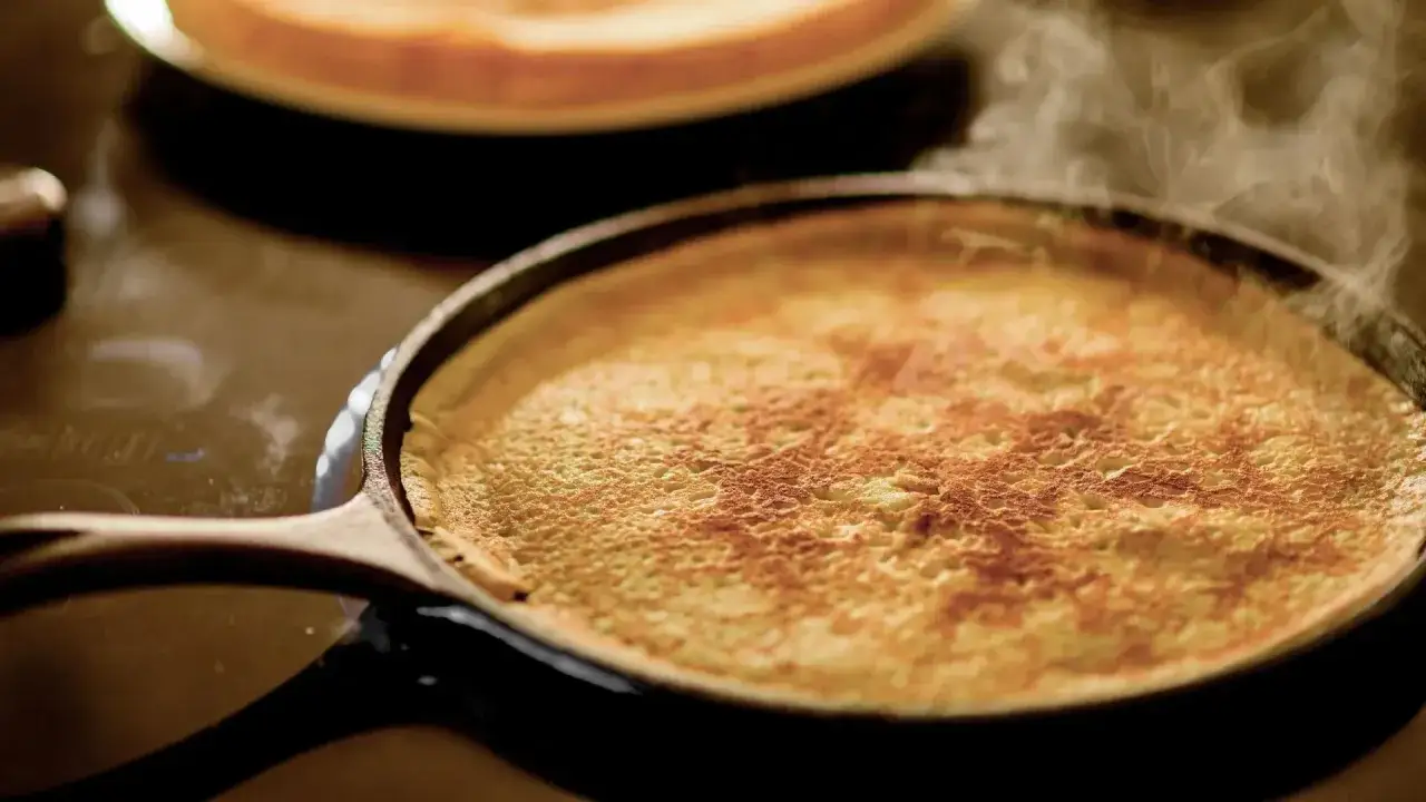 Ein goldbrauner Crêpe bräunt in einer Pfanne, Dampf steigt auf. Das perfekte crepes rezept für einen gemütlichen Morgen.