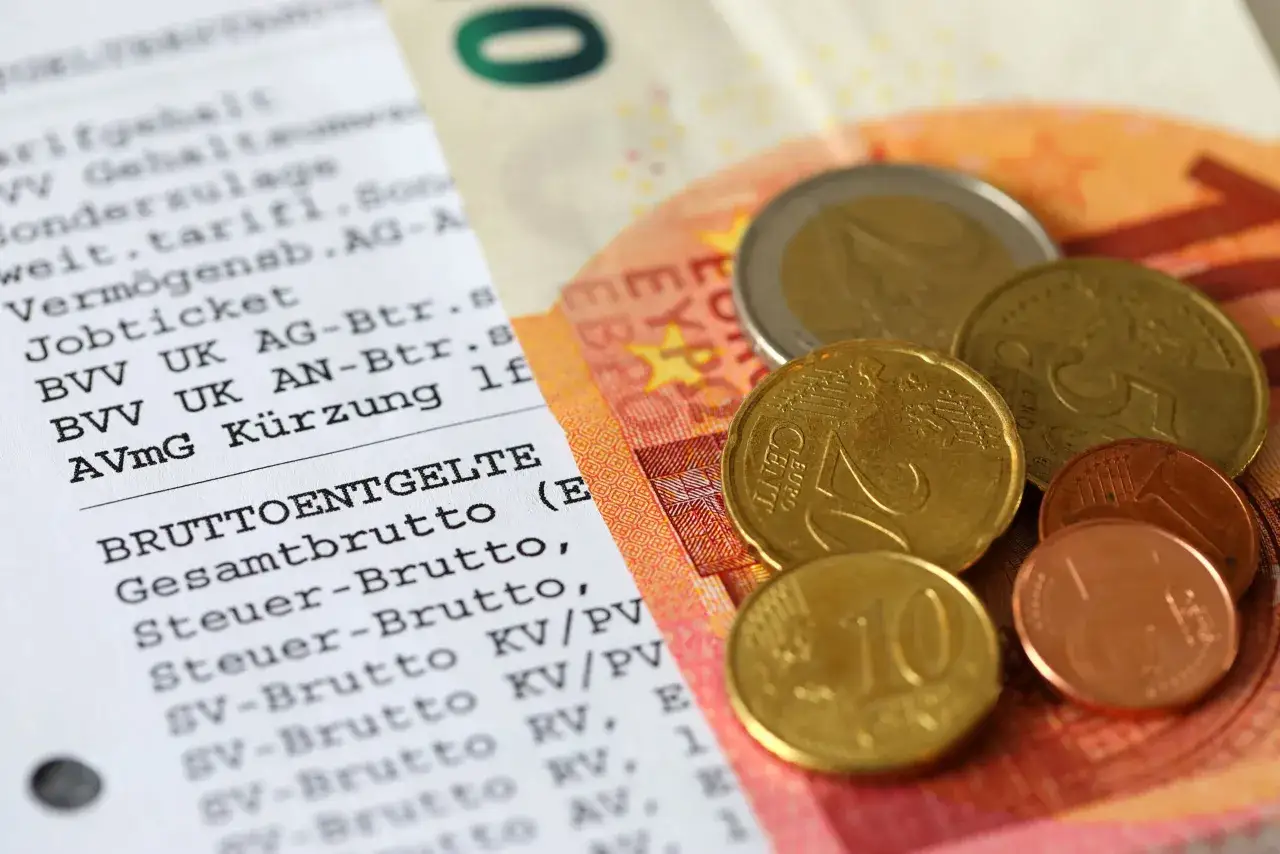 Lohnabrechnung mit Euro-Münzen und Geldschein. Hier wird deutlich, was sind Werbungskosten, die vom Bruttogehalt abgezogen werden können.